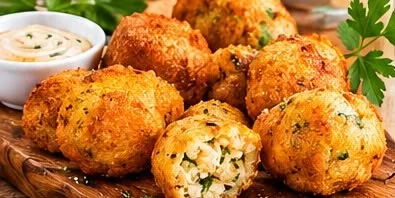 Porção de bolinhos dourados sobre tábua de madeira, um deles aberto mostrando o recheio